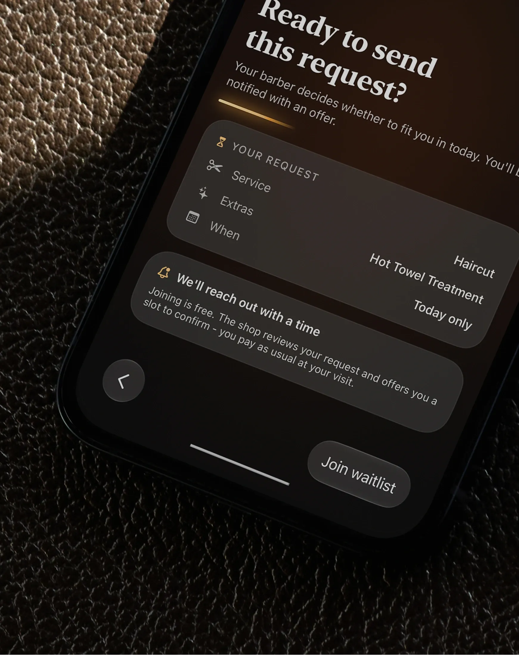 A booking request ready to send, on a phone face-up on leather - the service, the extras and the day, and what happens after the barber sees it
